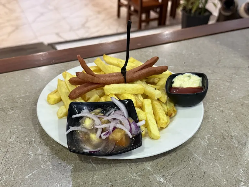 Salchipapa con curtido de cebolla y salsas